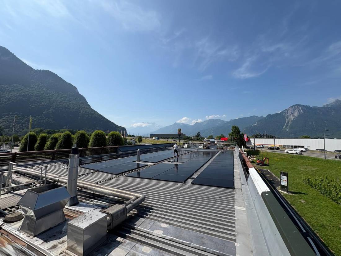 Champ de panneaux solaires posés sur le toit plat d'un bâtiment commercial avec chaîne de montagnes suisse