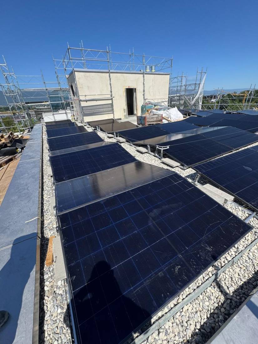 Champ de panneaux solaires sur le toit plat d'un immeuble en construction avec lestage gravier à Genève