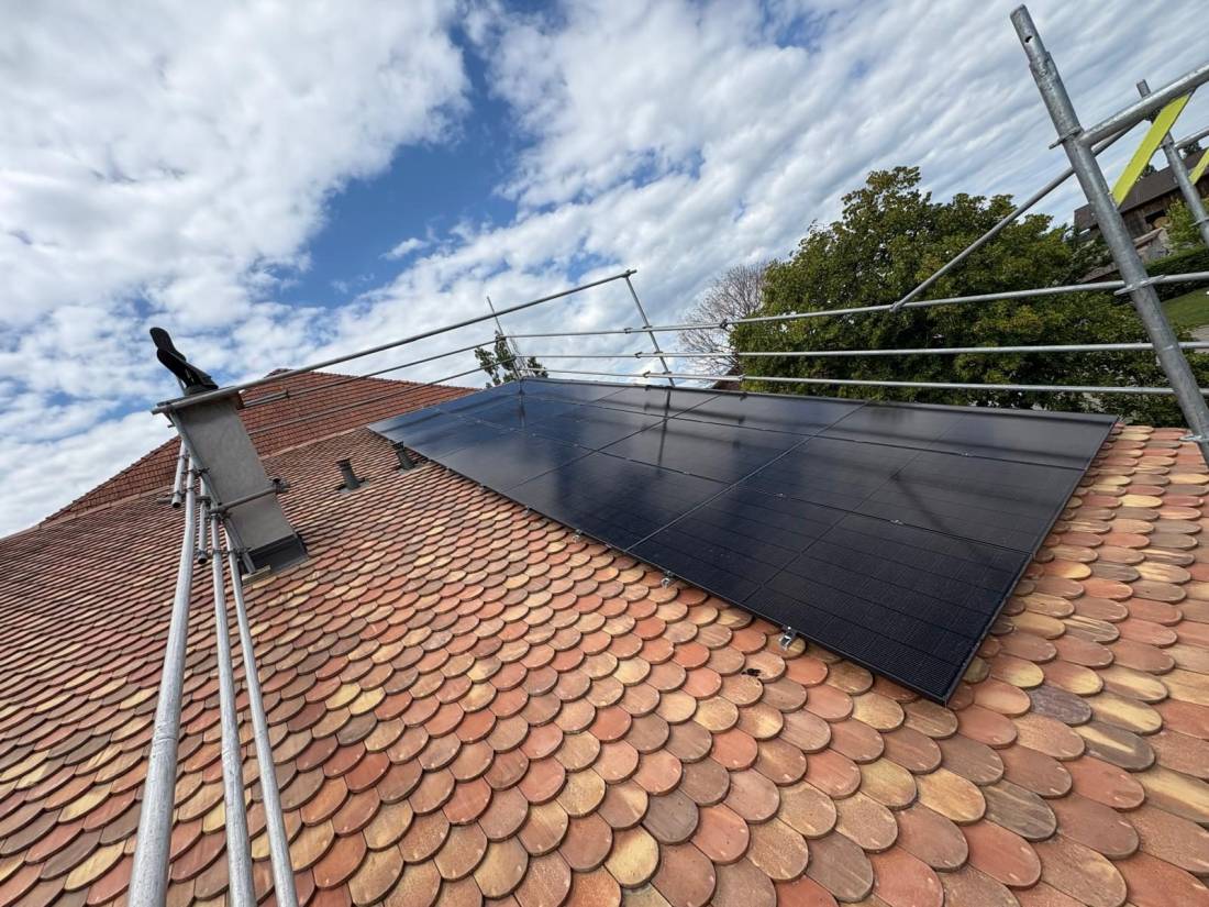 Installation de panneaux solaires full black sur toit en tuiles écaille avec cheminée et échafaudage en Suisse