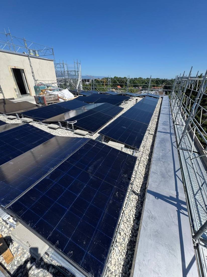 Installation de panneaux solaires sur toit plat lesté au gravier avec échafaudage de chantier à Genève