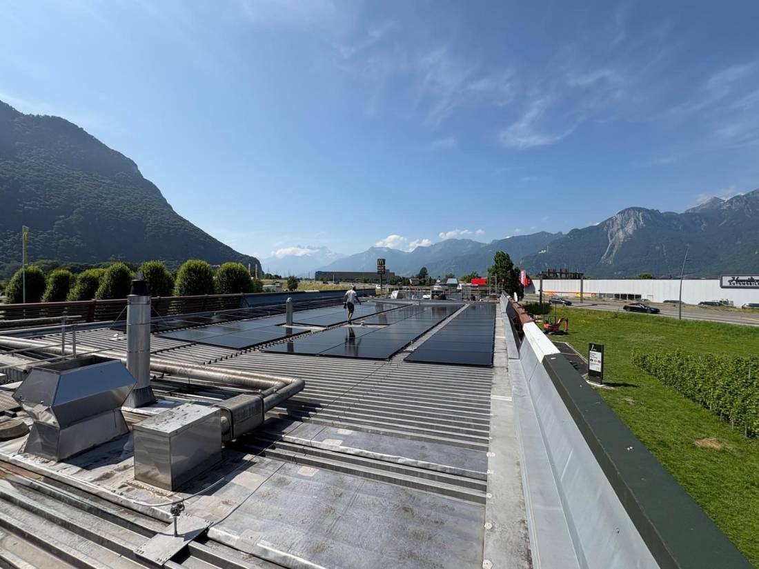 Installation de panneaux solaires sur toiture plate d'un bâtiment commercial entouré de montagnes en Valais