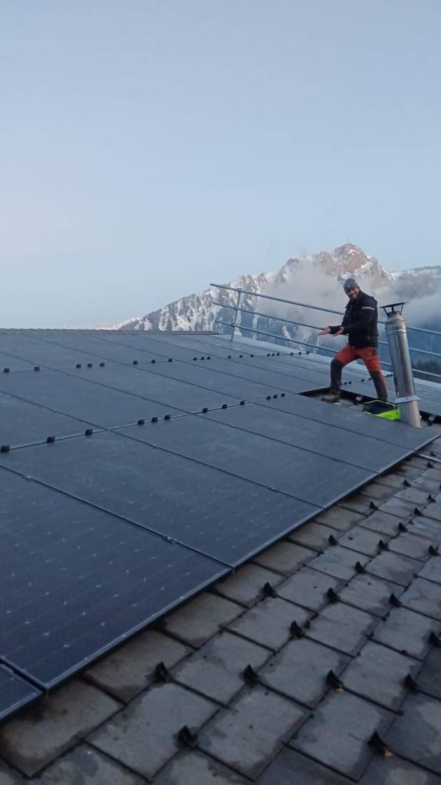 Installateur sur un chalet équipé de panneaux solaires face à des sommets enneigés en montagne suisse