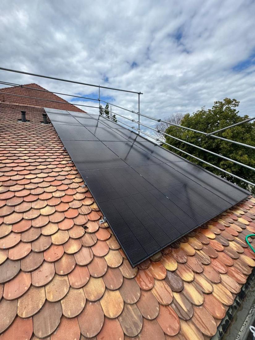 Panneaux solaires full black sur toiture en tuiles écaille vue en contre-plongée avec ciel nuageux