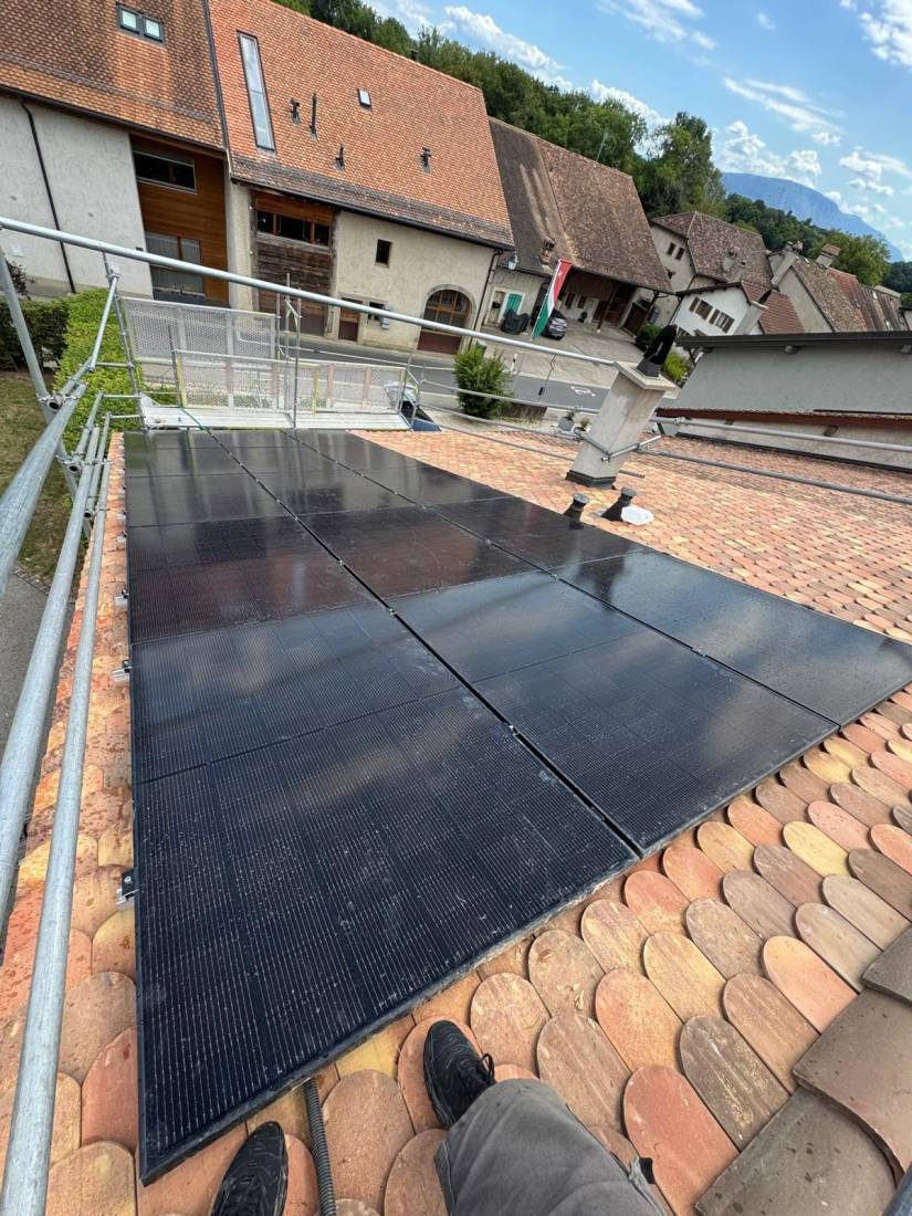 Panneaux solaires full black installés sur toiture en tuiles d'une ferme de village en Suisse romande
