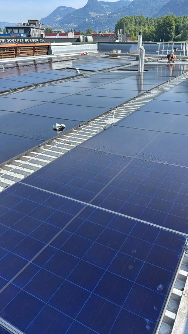Gros plan de panneaux photovoltaïques sur toiture plate de commerce avec montagnes du Valais en arrière-plan