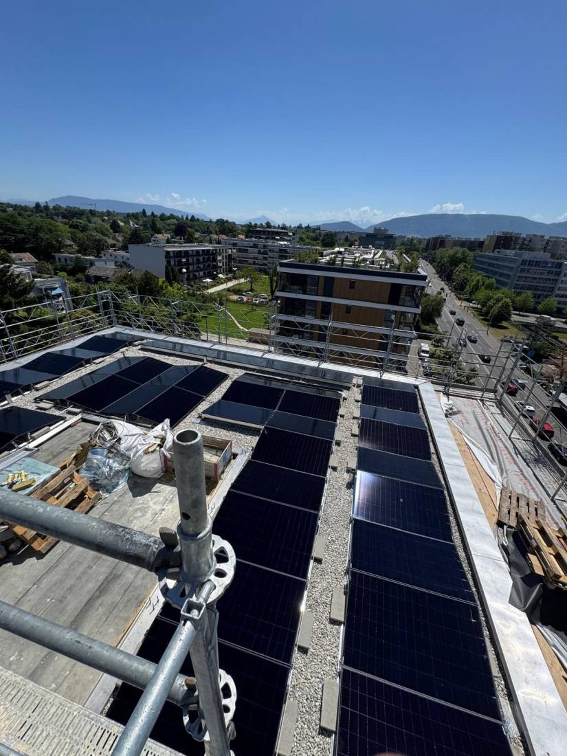 Panneaux solaires sur toit plat d'immeuble dominant la ville avec montagnes à l'horizon à Genève