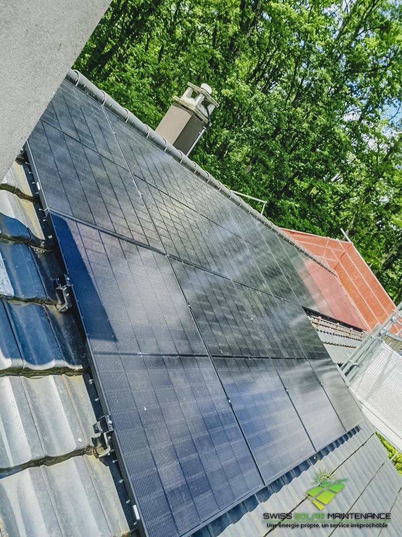 Champ de panneaux solaires sur toit en tuiles entouré de végétation en Suisse romande