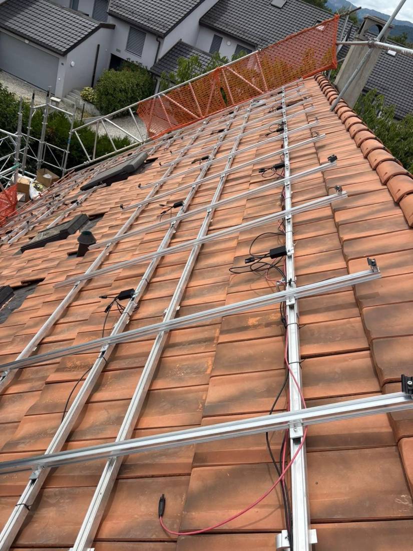 Pose des rails de fixation et du câblage de panneaux solaires en cours sur une toiture en tuiles