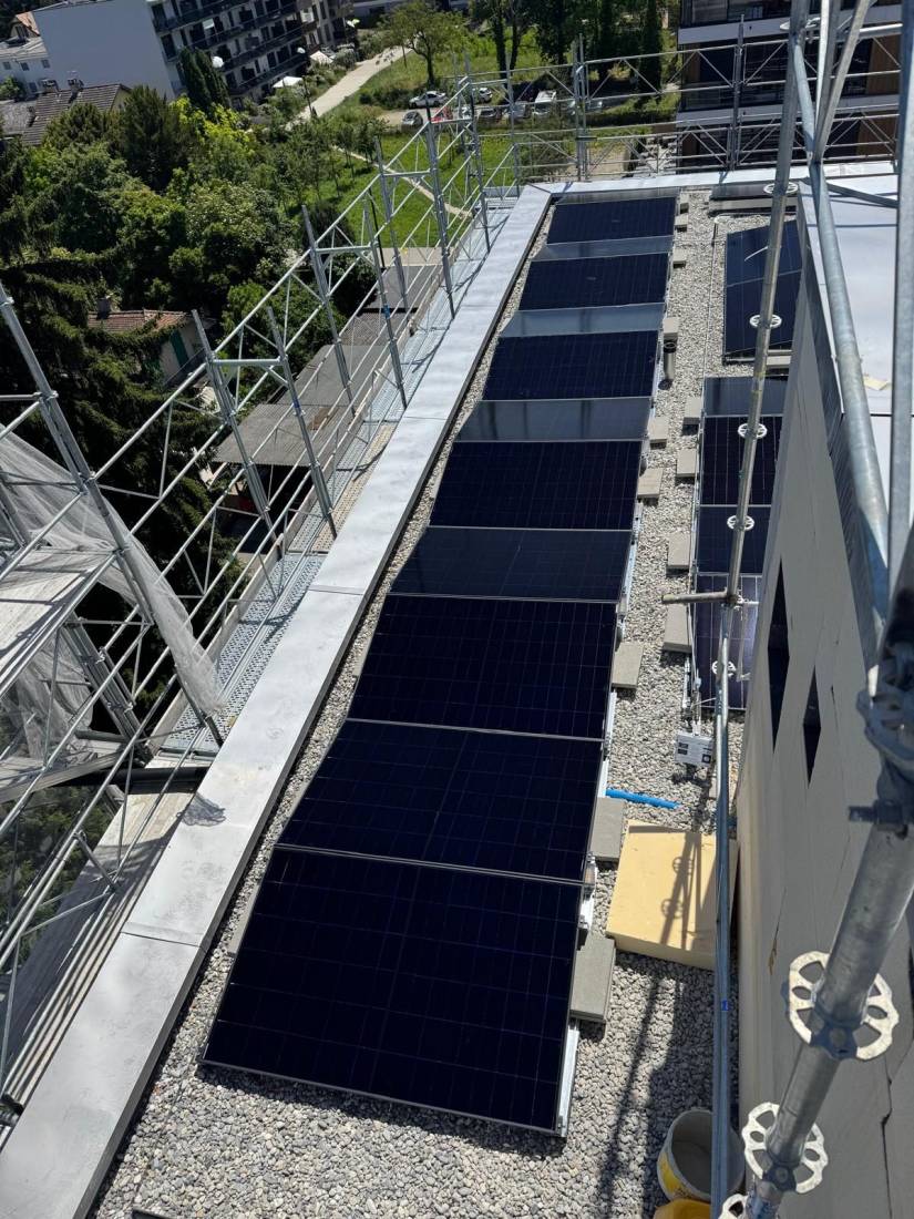 Longue rangée de panneaux solaires lestés au gravier le long du toit plat d'un immeuble en Suisse